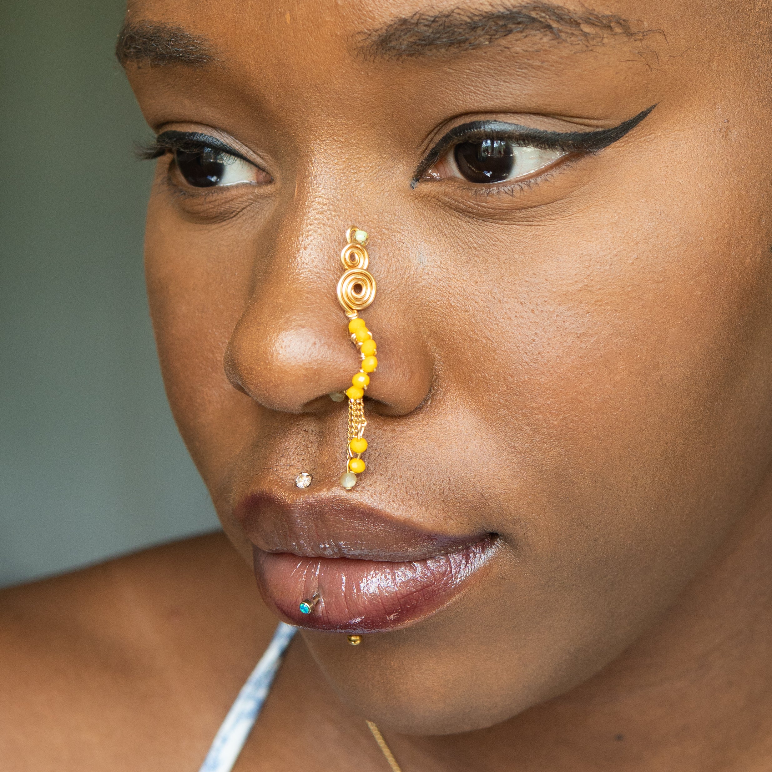 A gold-toned faux dangle nose ring cuffs the model's nostrils. Yellow transparent seed beads are wire-wrapped around the hoop's circumference, with three beaded gold curb chains dangling down.