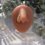 A light gold-toned faux nose piercing cuffs the model's nostril. The wire design forms an abstract spiral shape with three seed beads (yellow and pink) intertwined into the design.