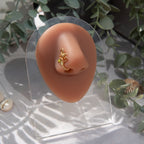 A gold-toned faux nose piercing cuffs the model's nostril. The wire design forms an abstract spiral shape with three green seed beads intertwined into the design.