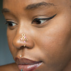 A gold-toned faux nose piercing cuffs the model's nostril. The wire design forms an abstract spiral shape with three pink seed beads intertwined into the design.