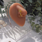 A light gold-toned faux nose piercing cuffs the model's nostril. The wire design forms an abstract spiral shape with three seed beads (yellow and pink) intertwined into the design.