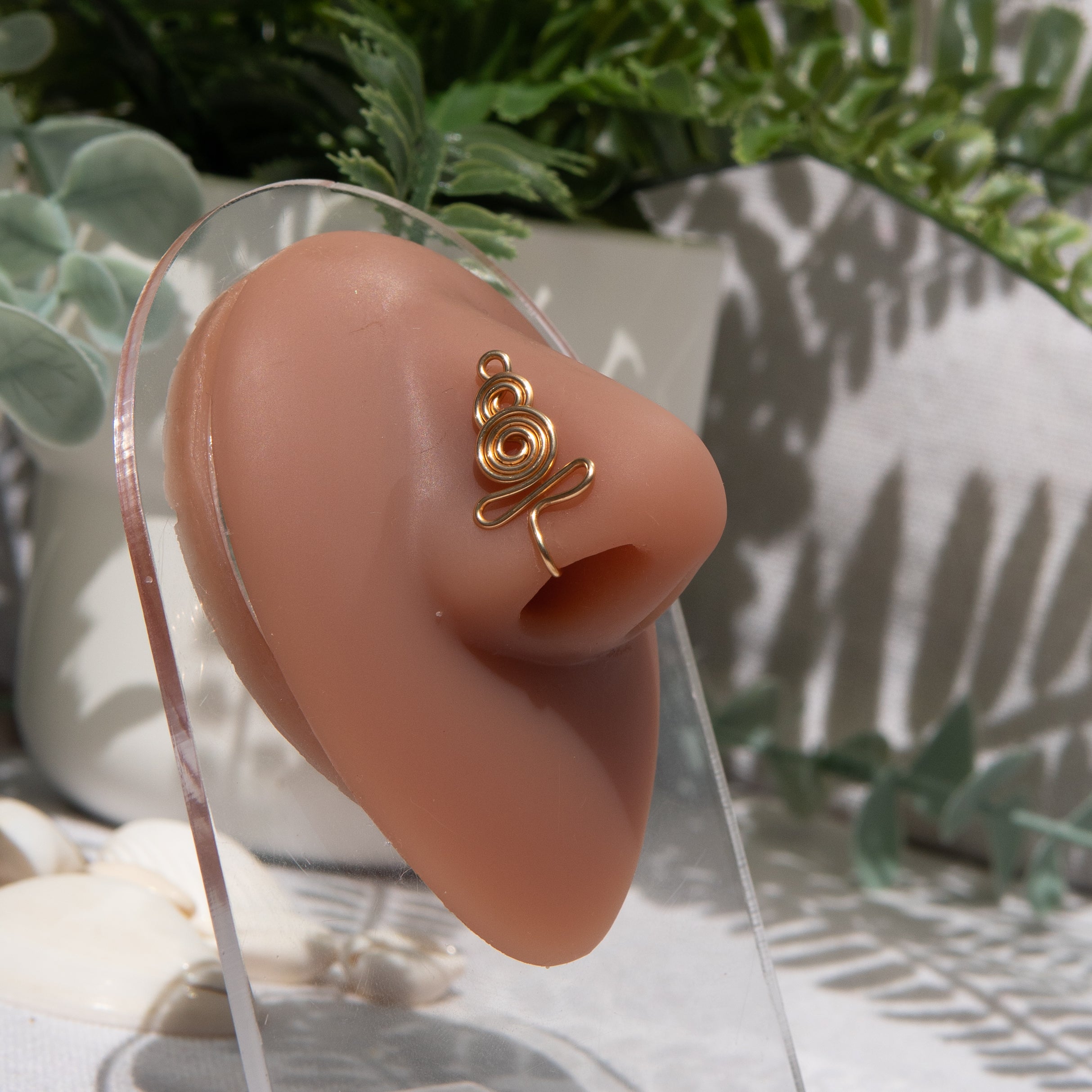 A gold-toned nose cuff adorns the model's nose in a circular wire design that spirals up and gradually decreases in size.