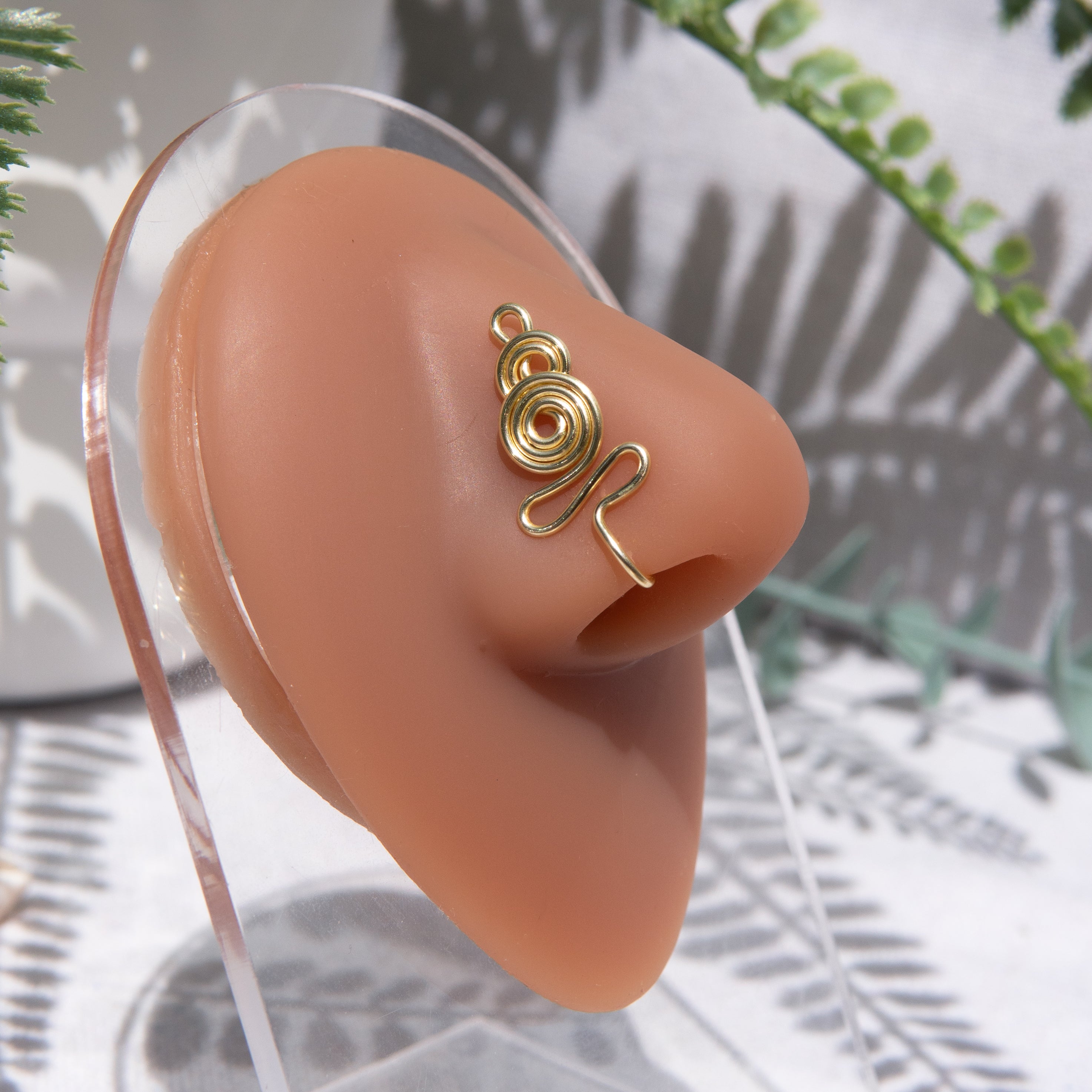 A light gold-toned nose cuff adorns the model's nose in a circular wire design that spirals up and gradually decreases in size.