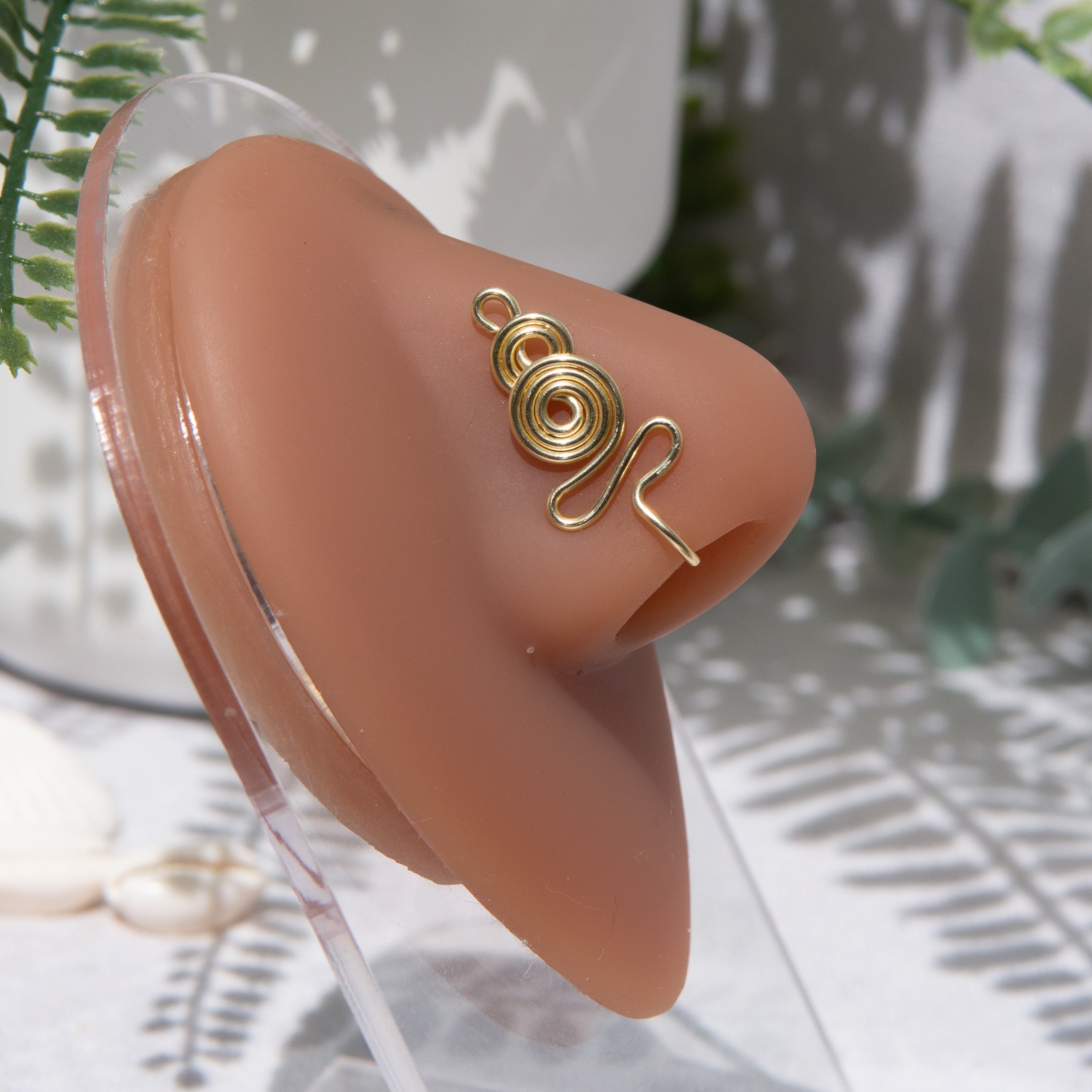 A light gold-toned nose cuff adorns the model's nose in a circular wire design that spirals up and gradually decreases in size.