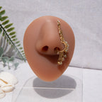 A gold-toned faux dangle nose ring cuffs the model's nostrils. Ombre nude seed beads are wire-wrapped around the hoop's circumference, with three beaded gold chains dangling down. An elaborate wire design tightly spirals up the nose, decreasing in size, with two additional dangle chains.