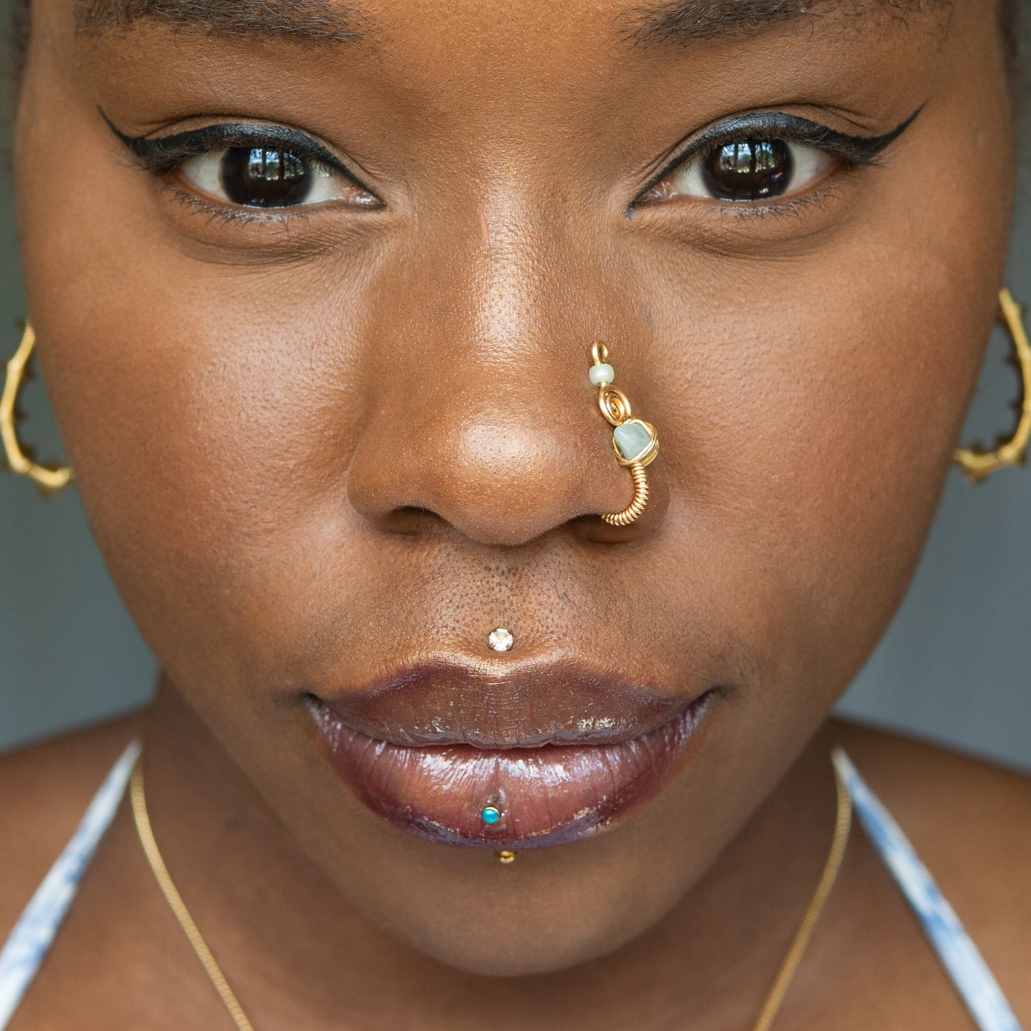 A gold-toned faux nose ring cuffs the model's nostril. A green aventurine crystal gemstone is wire-wrapped and interweaved into a vertical spiral wire design.