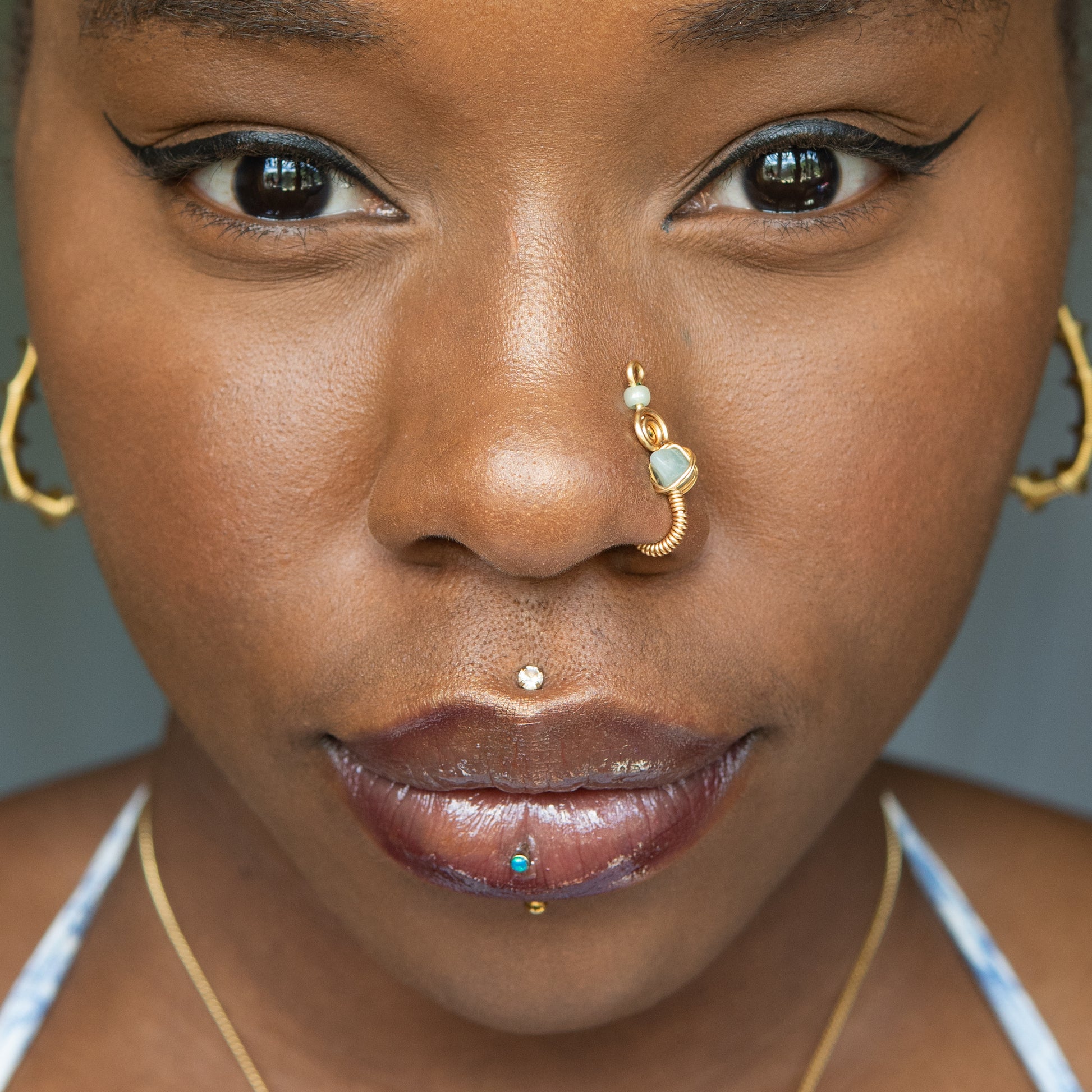 A gold-toned faux nose ring cuffs the model's nostril. A green aventurine crystal gemstone is wire-wrapped and interweaved into a vertical spiral wire design.