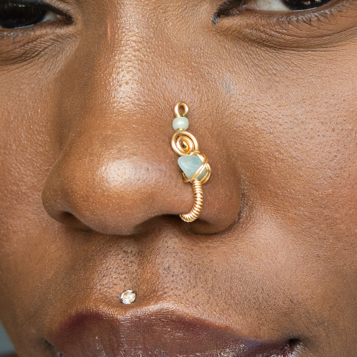 A gold-toned faux nose ring cuffs the model's nostril. A green aventurine crystal gemstone is wire-wrapped and interweaved into a vertical spiral wire design.