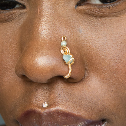 A gold-toned faux nose ring cuffs the model's nostril. A green aventurine crystal gemstone is wire-wrapped and interweaved into a vertical spiral wire design.