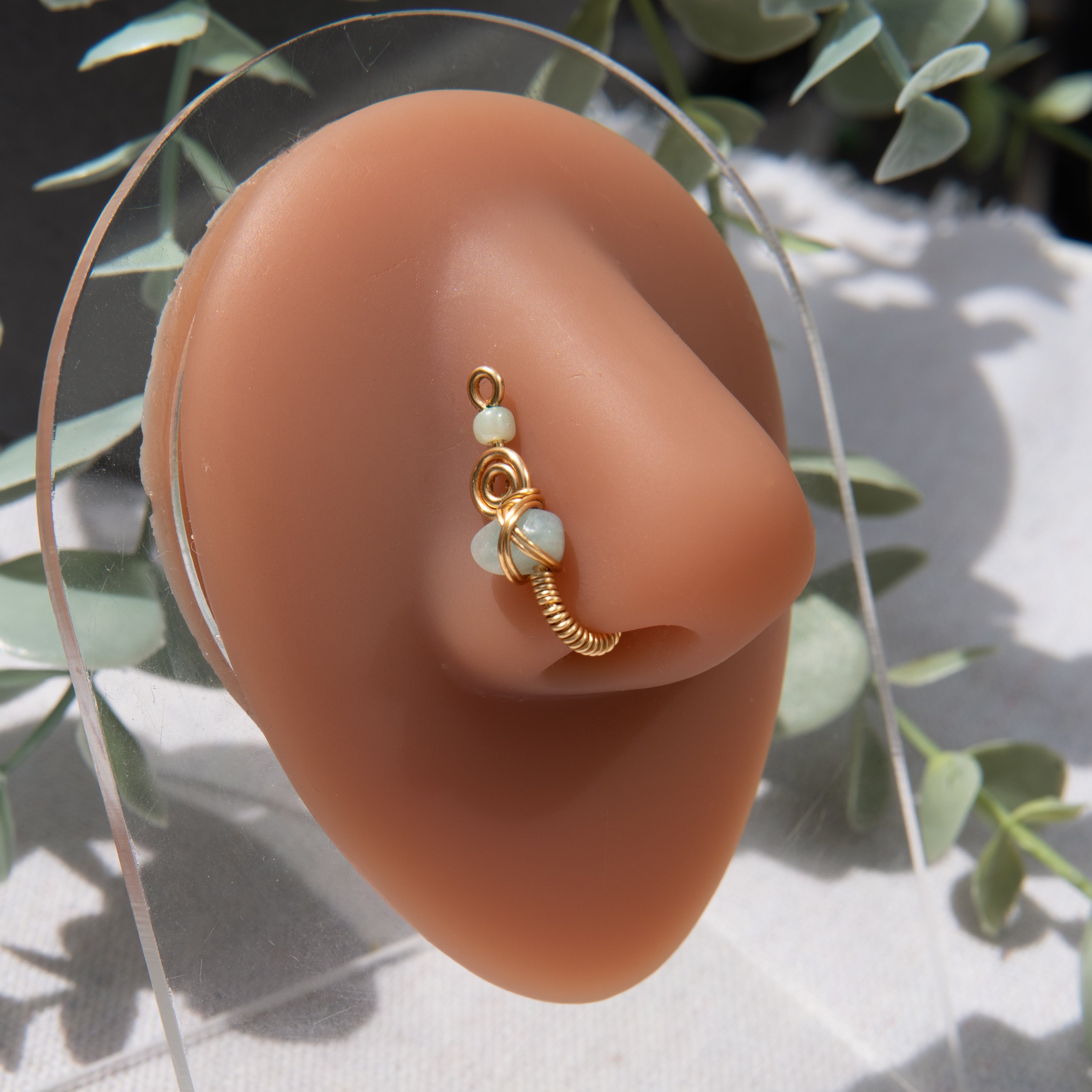 A gold-toned faux nose ring cuffs the model's nostril. A green aventurine crystal gemstone is wire-wrapped and interweaved into a vertical spiral wire design.