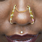 A two-toned faux bridge nose piercing in gold cuffs both nostrils of the model. Two dainty 18K gold-plated curb chains rest across the bridge of the nose, attached to the top of each nose cuff. Three seed beads are interweaved into the design of each nose cuff.
