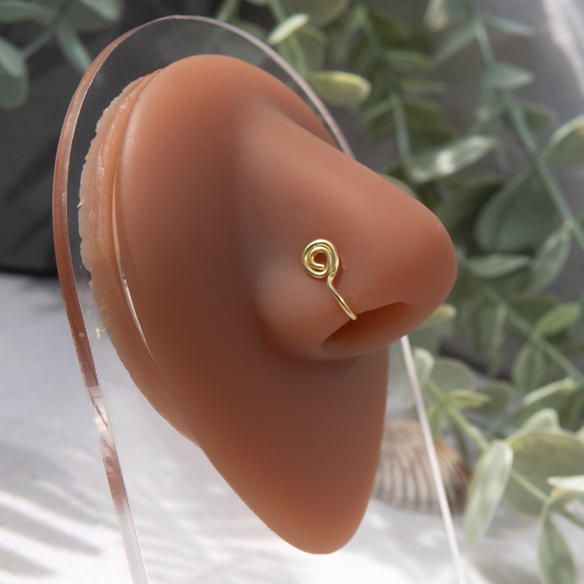 A gold-toned faux nose ring cuffs the model's nose. The wire design is shaped into a circular form.