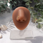 A gold-toned faux nose ring cuffs the model's nose. The wire design is shaped into a circular form.