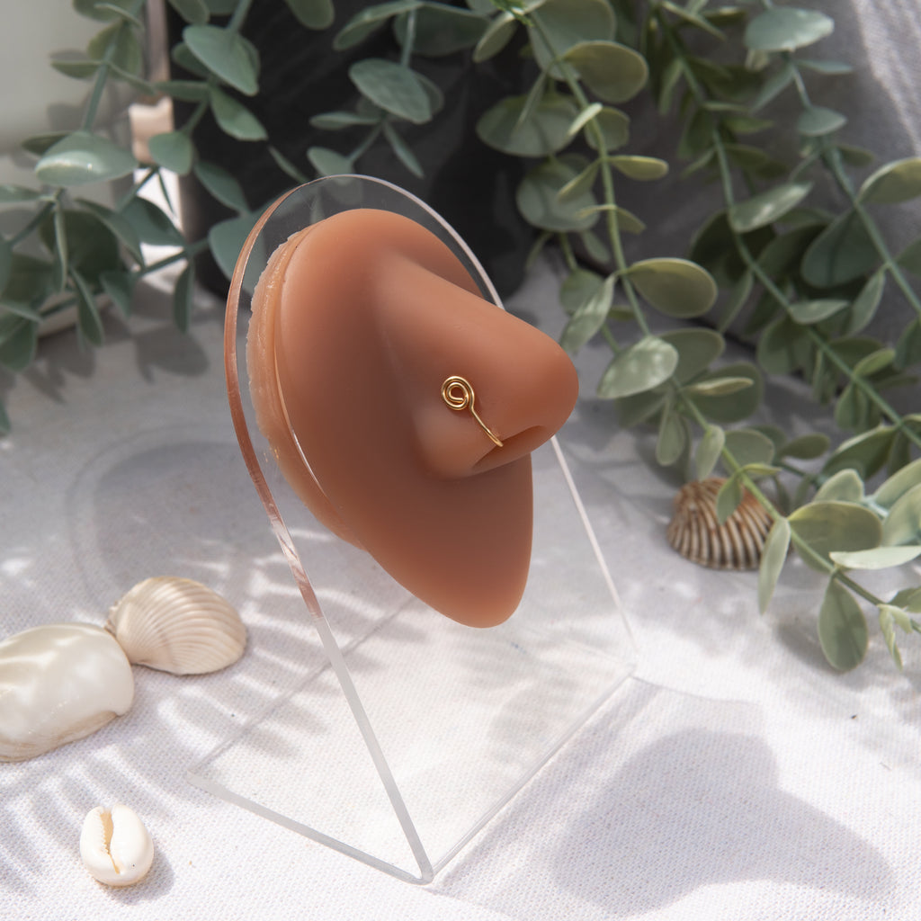 A gold-toned faux nose ring cuffs the model's nose. The wire design is shaped into a circular form.