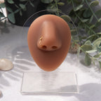 A gold-toned faux nose ring cuffs the model's nose. The wire design is shaped into a circular form.