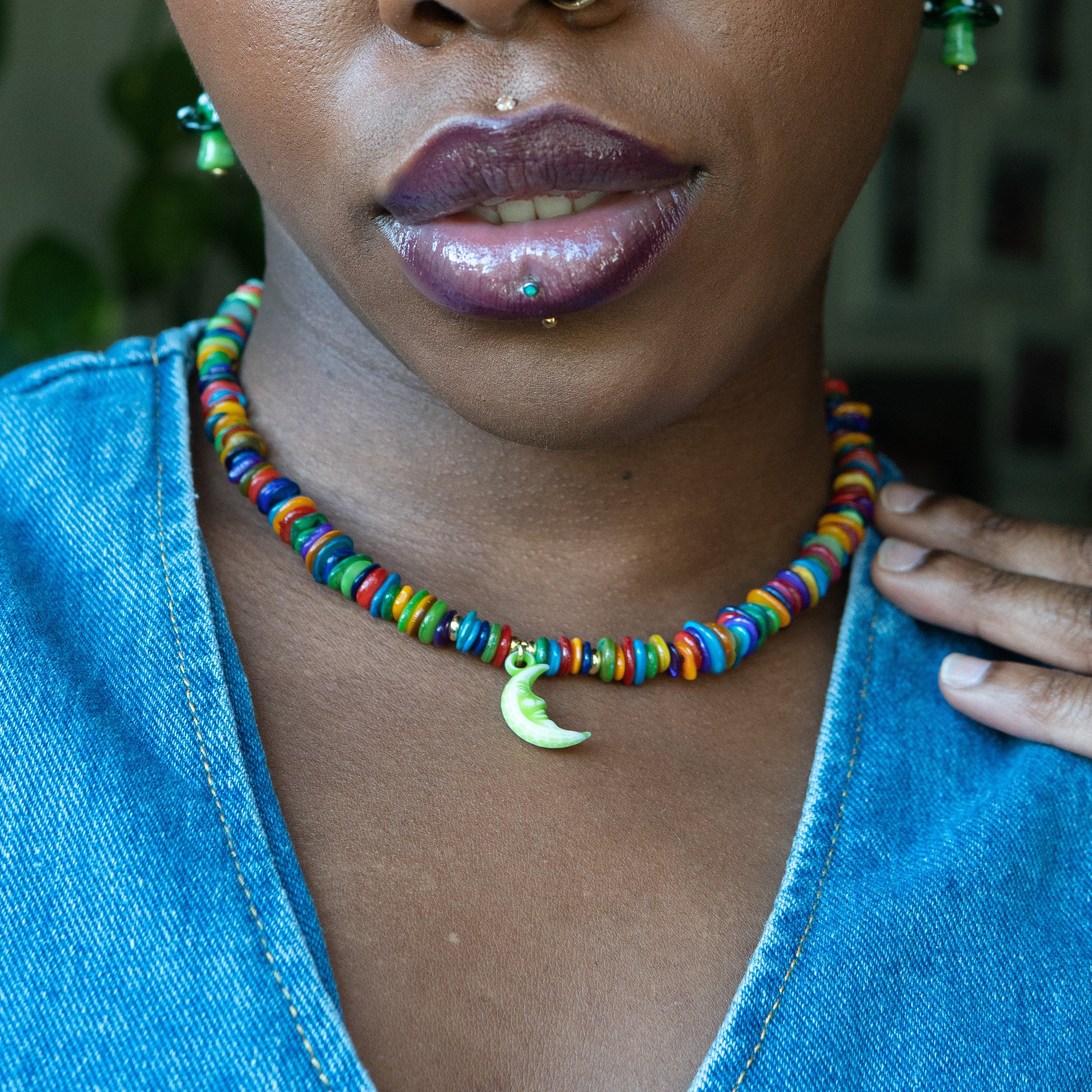 Person wearing a colorful beaded necklace with a blue top and green earrings.