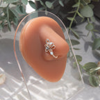 A silver fake nose piercing cuffs the model's nostril. The wire design forms an abstract spiral shape with three blue seed beads intertwined into the design.