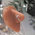 A silver fake nose piercing cuffs the model's nostril. The wire design forms an abstract spiral shape with three blue seed beads intertwined into the design.